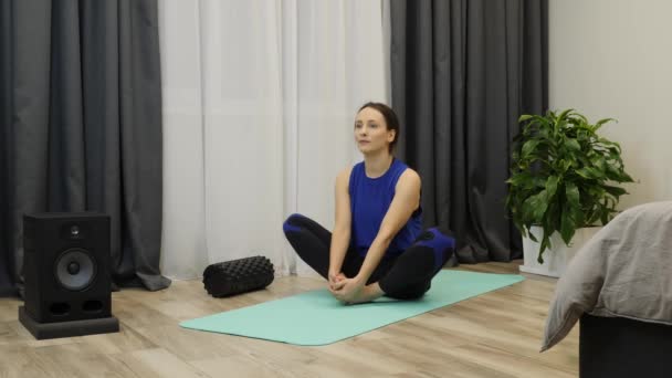 Mulher alonga os músculos e fazendo ioga posar no tapete. Feminino faz exercícios de alongamento em casa na sala de estar brilhante. Menina praticando ioga e exercícios de fitness — Vídeo de Stock