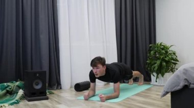 Erkek sporcu paspasın üzerinde tahta pozu verir. Genç formda adam günlük egzersizlerinin bir parçası olarak kalas yapıyor. Siyah elbiseli spor hocası tahta pozisyonunda duruyor. Egzersiz konsepti