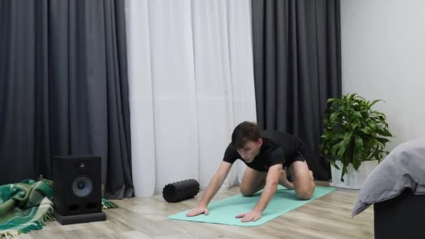 Genç sporcu, kalça kaslarını esnetir ve yoga minderinde diz kapağı kaslarını çalıştırır. Bacak kaslarını çalıştıran sportif bir adam. Esneme hareketleri ve yoga egzersizleri yapan Kafkas erkek fitness eğitmeni. Sağlıklı yaşam tarzı kavramı — Stok video