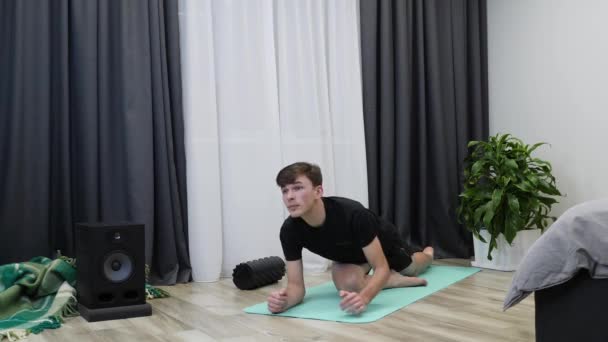 Man stretchar efter hård inomhusträning. Ung hane fitness instruktör sträcker ut benmusklerna, glutealmusklerna på yogamattan. Idrottaren tränar fitness och stretchar. Pojkträning i yoga — Stockvideo