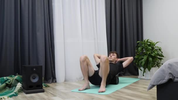 Fit male massages spine muscles using fascia roll. Boy does myofascial release massage with roller. Motivated caucasian young man in black shorts and t-shirt does relaxing and rehab exercises at home — Stock Video
