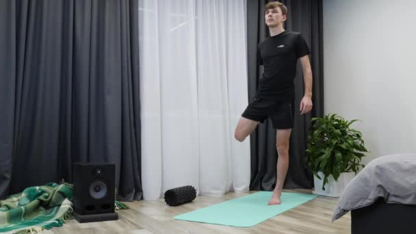 Молодий спортсмен розтягує м'язи ніг на йога мат вдома. Вмістити мотивовану людину, що розтягується в приміщенні. Інструктор з фітнесу показує аеробні та розтяжні вправи. Концепція домашньої фітнесу. Тренувальні вправи — стокове відео