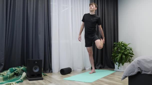 Člověk před cvičením cvičí. Mladý atletický muž cvičí na józe. Chlapec v černém sportovním oblečení protahuje svaly. Fitness trenér ukazuje aerobní cvičení doma — Stock video