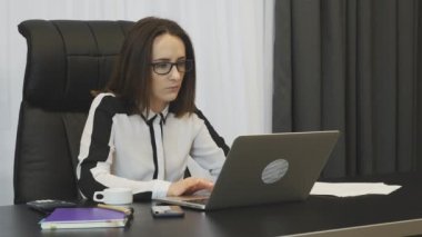 Woman typing on laptop in office. Concentrated lady boss in white blouse working at office. Collected brunette female works at working place. Businesswoman works on laptop in modern office