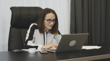 Happy business woman celebrating good news seen on laptop. Successful young woman excited with financial results on trading stock market. Trader won money on stocks. Smiling female showing yes sign