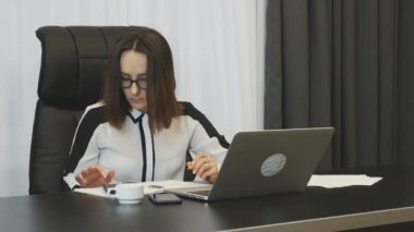 Woman is considering company expenses in office. Businesswoman keeps accounts at work. Confident concentrated female works in office. Brunette lady doing job. Business concept