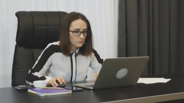 Female concentrated at work. Woman works on laptop using computer mouse in modern office. Lady boss working in her office. Businesswoman doing job. Business victory concept