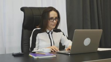 Happy female boss raising her arms and applauds at workplace. Business woman excited with successful company deal. Woman looking at laptop and enjoying with results in stocks financial market