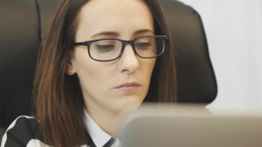 Tired female face working on laptop in office in the evening. Close up of woman takes off glasses after hard working day. Portrait of girl overworked at workplace. Woman looking at computer screen