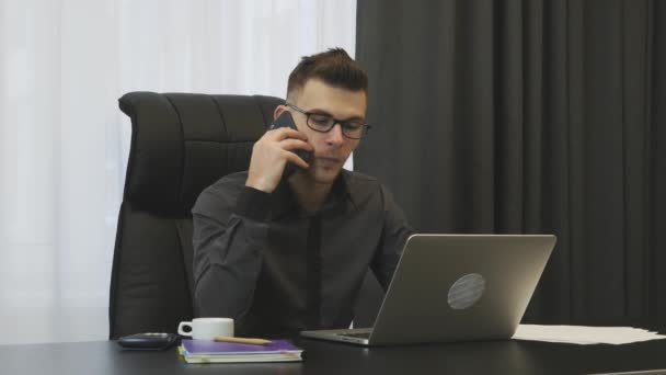 Man is calling on phone from modern office. Successful businessman talking on phone sitting at his office desk. Young smiling male broker speaking on phones with clients at workplace — 비디오