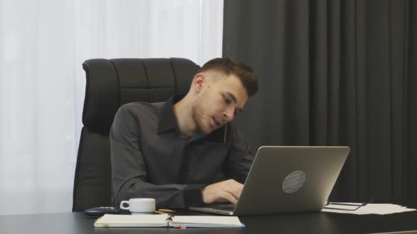 Man talking on phone in office. Businessman in glasses talks on smartphone in modern office. Man sitting at office desk and speaking with partners by phone. Young broker making deal on phone in office — Stok video