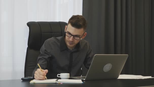 Facet pisze na klawiaturze laptopa w biurze. Udany biznesmen pracujący na komputerze w biurze. Mężczyzna patrzy na ekran laptopa i robi notatki. Pewny siebie człowiek uważa zarobki firmy w miejscu pracy — Wideo stockowe