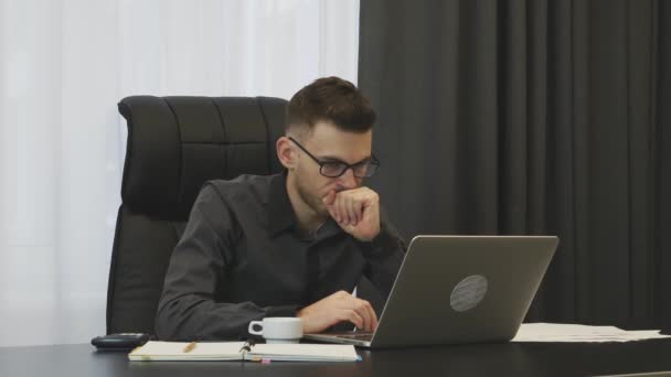 Male concentrated on work in modern office. Focused businessman working at office. Young confident man works on laptop at workplace.  Man in suit and glasses thinking about his job. Business concept — Stockvideo