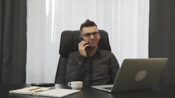 Επιτυχημένος νεαρός επιχειρηματίας μιλάει στο τηλέφωνο στο σύγχρονο γραφείο του. Ο άνθρωπος μιλάει με συνεργάτες στο smartphone και κάνει συμφωνία. Άνδρας χρηματοδότης μιλάει στο τηλέφωνο κάθεται στο γραφείο του. Επιχειρηματική έννοια — Αρχείο Βίντεο