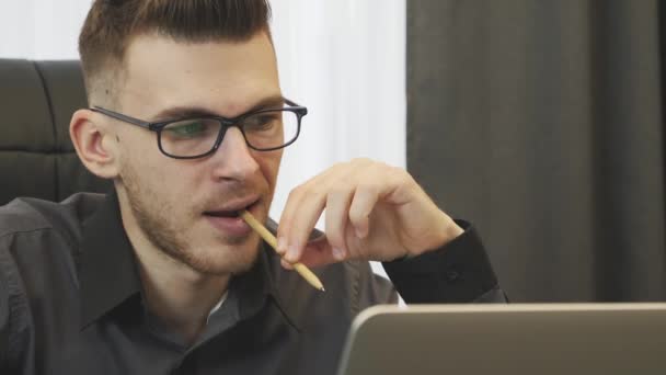 A férfi a laptop képernyőjére néz, közelről. Egy szemüveges üzletember dolgozik a modern irodájában. Egy férfi portréja a képernyőn. A vállalat igazgatója pénzügyi jelentést olvas laptopon — Stock videók
