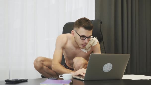 Man kraken in stoel werkt op laptop in het kantoor. Man in ondergoed typen op laptop toetsenbord op het werk. Jonge makelaar zit op kraakpand in zijn kantoor en leest nieuws op internet — Stockvideo