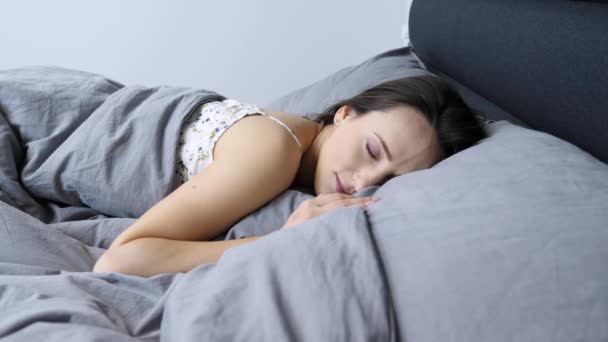 Mujer acostada en la cama y sonriente, retrato. Cara femenina joven sonriendo a la cámara, vista de cerca. Chica tímida en ropa interior se encuentra en la cama y sonríe. Mujer se despierta en la cama por la mañana y tímido — Vídeo de stock