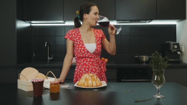 A nő bort iszik otthon, a modern konyhában. Fiatal, gyönyörű nő házi készítésű pitét készített és vörösbort ivott. Háziasszony portré a professzionális konyhában. Egészséges életmód és élelmiszer-koncepció — Stock videók