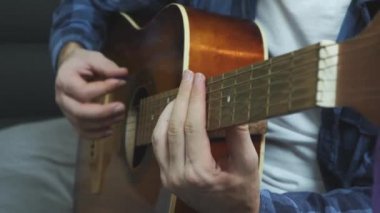 Erkek elleri gitar penasıyla akustik gitar tıngırdatıyor. Akustik gitarla balad çalan adam