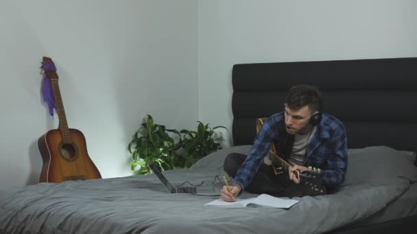 Muzicianul a creat un cântec nou la chitara electrică. Tineri mileniali practicând chitara pe pat în camera de zi modernă. Omul cântă muzică lirică la instrumentul muzical. Lecţii de chitară. Conceptul muzical — Videoclip de stoc