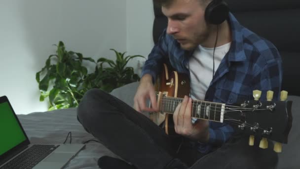 Egy férfi fejhallgatóban elektromos gitáron játszik, közelről. Férfi zeneszerző, aki új dalszöveget ír. Közelről láthatod a gitárt. A gitáros új akkordokat gyakorol. Zenei koncepció — Stock videók