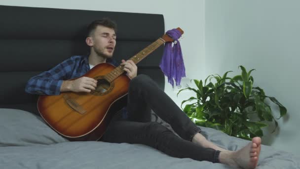 Adam evde, yatakta akustik gitar çalarken şarkı söylüyor. Müzik konsepti — Stok video