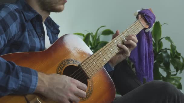 Giovane musicista barbuto che suona assolo di chitarra solista sulla chitarra acustica seduto sul letto a casa a esercitarsi per un concerto dal vivo . — Video Stock