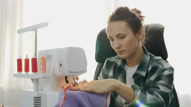 Ritratto di giovane donna che cuce tessuto viola con macchina da cucire. Le mani di donna cuciono un vestito. Moda, creazione e sartoria — Video Stock