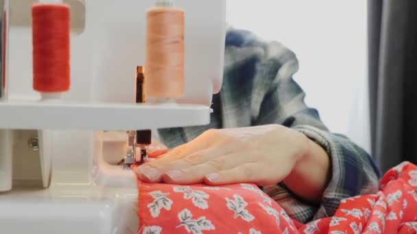 Flickan syr på symaskinen. Ung kvinna som arbetar med symaskin, närbild. Workshop i sytyg. Kvinnliga händer syr på overlock. Skapa och skräddarsy klädkoncept — Stockvideo