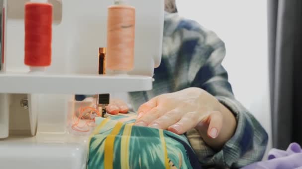 在缝纫面料方面，妇女的双手紧握在一起工作。缝纫机的特写。上锁机的细节。女的在缝衣服。创造和裁剪服装概念 — 图库视频影像