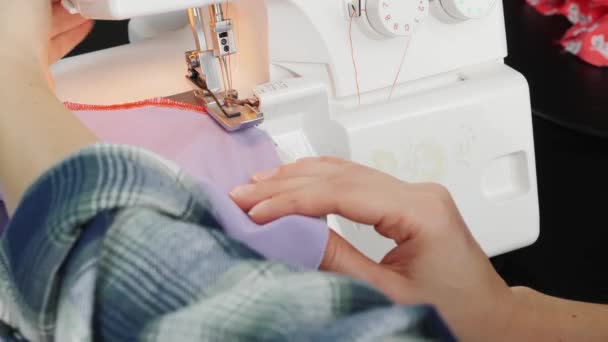 Додатково крупним планом руки жінки пришивають край тканини на швейній машинці. Подробиці оверлокатора. Жінка-дизайнер працює на швейній машині. Створення та пошиття одягу — стокове відео