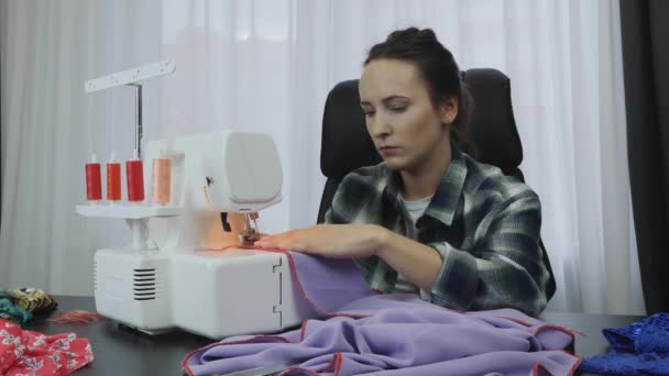 Жінка працює на оверлоку в студії кравця. Швачка пришиває тканину на швейній машинці. Портрет жінки, яка працює і створює плаття. Концепція моди. Створення та пошиття одягу — стокове відео