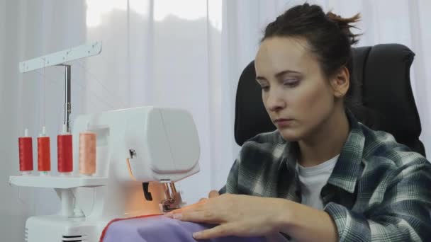 Primer plano de la cara de la mujer trabajando en la máquina de coser. Retrato de la costura femenina en overlock. Taller en tejido de coser. Creación y confección de ropa en el estudio del sastre — Vídeos de Stock