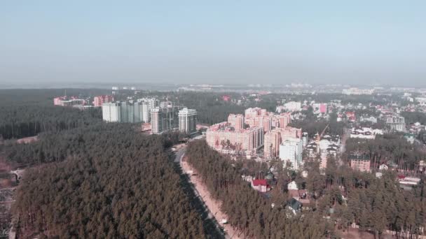 Il drone vola sopra nuovi edifici circondati dalla foresta. Vista aerea dall'alto della città con grattacieli. Filmato aereo drone di costruzione in città con alberi di pino — Video Stock