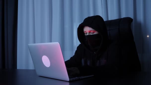 Vrouwelijke hacker zit in de donkere kamer en typt op laptop toetsenbord. Vrouw in zwart masker en kap codering op het scherm en het breken van wachtwoord. Professionele hacker breekt sociale web beveiliging bescherming — Stockvideo