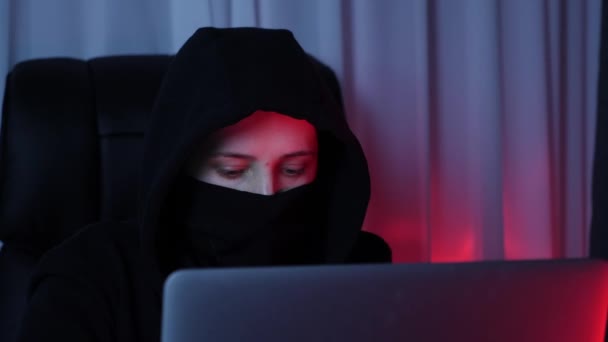 Frauengesicht in schwarzer Maske und Kapuzenpulli blickt auf Computerbildschirm und bricht Passwort. Junger Hacker bricht Sicherheitsschutz auf Laptop-Bildschirm Konzept des Online-Virenschutzes. Zeitlupe — Stockvideo