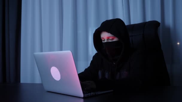 Mulher hacker sentado no quarto escuro e digitando no teclado do laptop. Mulher em máscara preta e capuz codificação na tela e quebrando senha. Hacker profissional quebra a proteção de segurança da web. Movimento lento — Vídeo de Stock