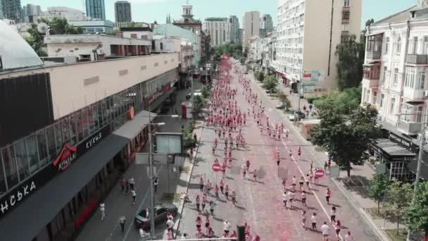 Kyiv/Ukraine - June 2, 2019 - People taking part in run competition "Color Run Kyiv". Drone flying above street with women and men running among city center. Happy participants at run race, drone view — стокове відео