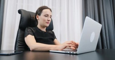 İşadamı kadın ofiste çalışıyor. Beyaz bir kadın dizüstü bilgisayarda klavyeyle yazı yazıyor ve ekrana bakıyor. Ofis masasında oturan siyah elbiseli kadın.