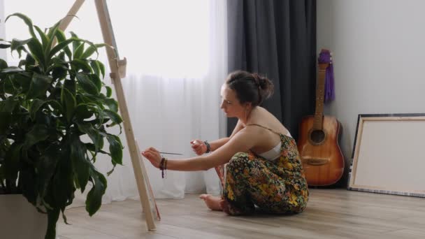 Mujer encantadora pinta una pintura sobre lienzo en taller atmosférico. Talentosa joven dibujo sobre lienzo en casa — Vídeos de Stock