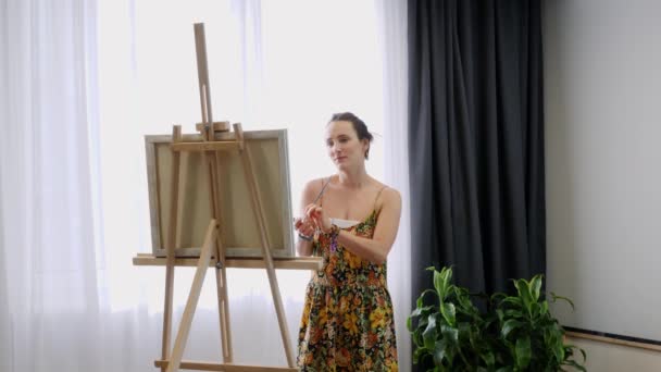 Молода талановита жінка малює на полотні в художній домашній студії. Жінка-художник стоїть біля мольберта і малює картину на полотні. Натхнення. Художня академія — стокове відео