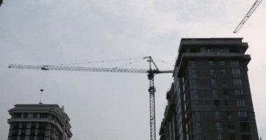 Gökdelenler yapım aşamasında. Turnalar yağmurlu bir günde gri bulutlu gökyüzünün altında inşaat sahasında çalışıyor.