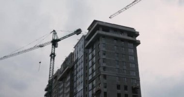 Yüksek vinç gökdelen şantiyesinde çalışıyor. Yeşil bölgede apartman inşaatı. Vinçle birlikte inşaat halindeki yüksek katlı yerleşim yeri