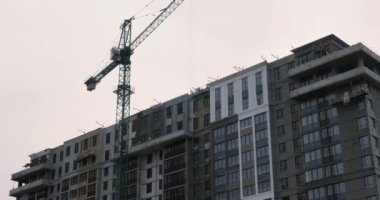 İnşaat alanında büyük bir vinç çalışıyor. Crane, gri bulutlu gökyüzüne karşı inşaat alanında çalışıyor. Yüksek gökdelenin inşaatı