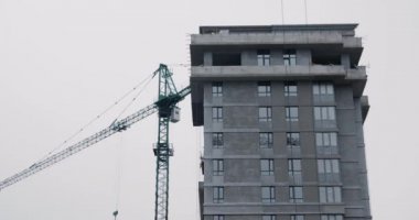 Yüksek inşaat vinci şantiyede çalışıyor. Vinç yapım aşamasındayken gökdeleni kapatın. Yüksek vinç evle birlikte inşaat alanında çalışıyor.