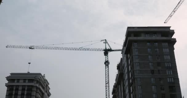 Drapacze chmur w budowie z ogromnymi żurawiami.Dźwigi pracujące na placu budowy pod szarym zachmurzonym niebem w deszczowe dni — Wideo stockowe