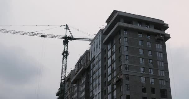 Yüksek vinçli inşaat alanı. İnşaatçılar modern konut kompleksi inşa ediyorlar. Crane, gri bulutlu gökyüzünün altında inşaat alanında çalışıyor. Gökdelen büyük bir vinçle yapım aşamasında. — Stok video