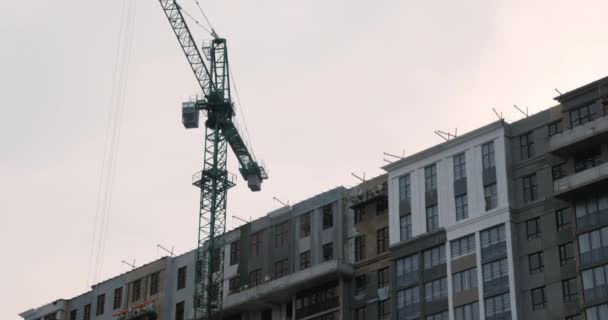Close-up de guindaste de alta construção no local de construção com arranha-céu não construído. Trabalhadores em uniforme construir um complexo residencial moderno — Vídeo de Stock