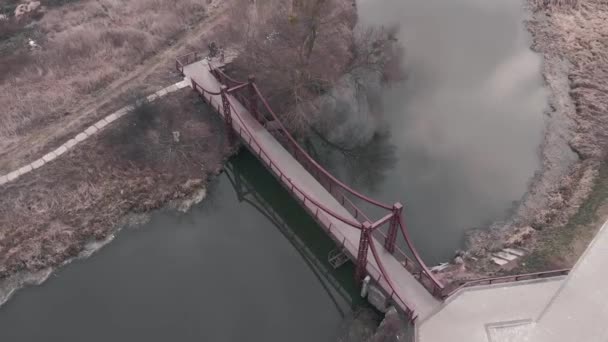 Luchtfoto van de voetgangersbrug over de rivier. Drone vliegt boven de stadskade met een bruggetje — Stockvideo