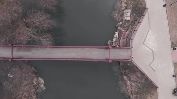 Frau läuft über Brücke über Fluss, Luftaufnahme. Sportlerin läuft über Stadtpromenade mit Brücke und Park. Laufkonzept — Stockvideo